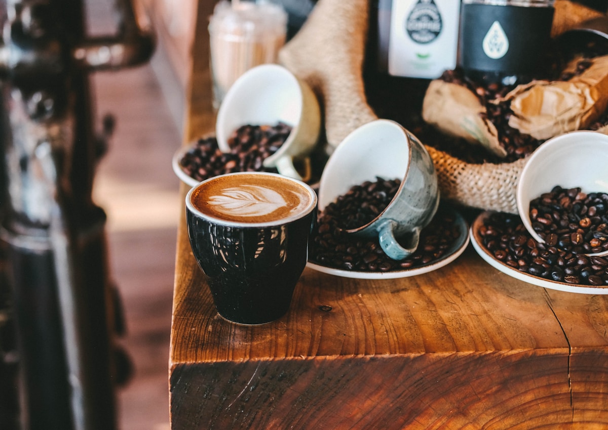 Fresh latte with leaf-shaped foam art and roasted coffee beans on a wooden table