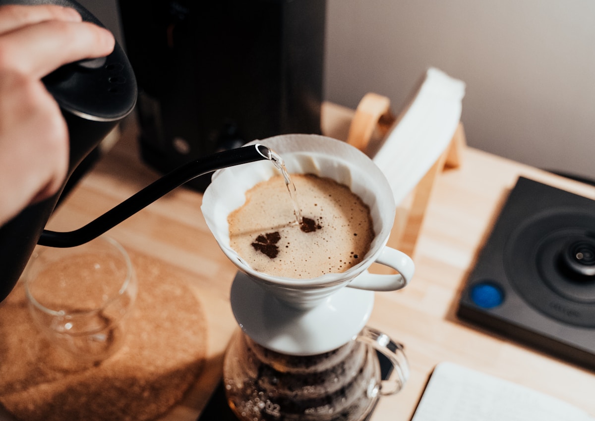 A black gooseneck kettle pouring hot water into a white ceramic coffee dripper